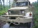 1990 Ford Bronco - A tan military truck is parked outdoors on a wet, wooded road.