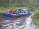 1995 Dodge 1500 - A blue pickup truck is stuck in a body of water, with two people inside and one in the truck bed.