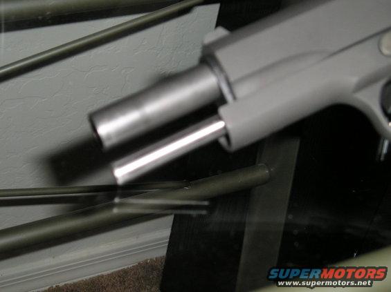 Close-up of a pistol barrel and slide, with metal rods in the foreground