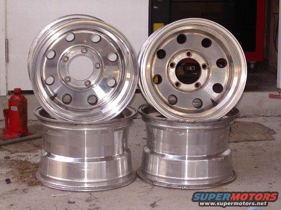 Two aluminum wheels stacked on top of two other aluminum wheels. A red hydraulic jack is to the left