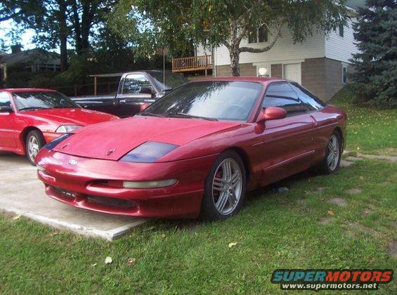 Red 1995 Ford Probe parked on grass, front 3/4 view, with a red car and a black truck behind it
