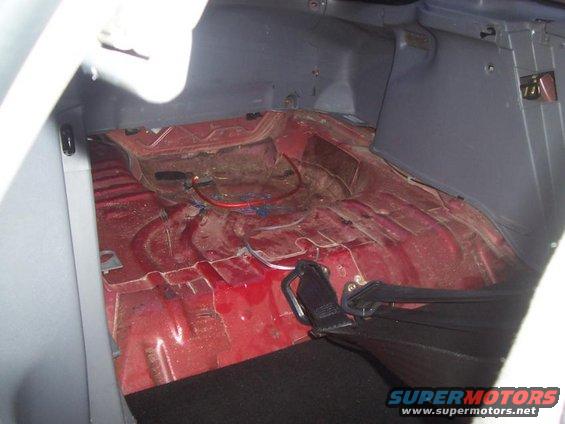 Empty car trunk with red painted floor and some wiring. Seatbelt buckle visible