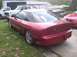 1995 Ford Probe - A red coupe is parked in a grassy area next to a white truck and other vehicles.