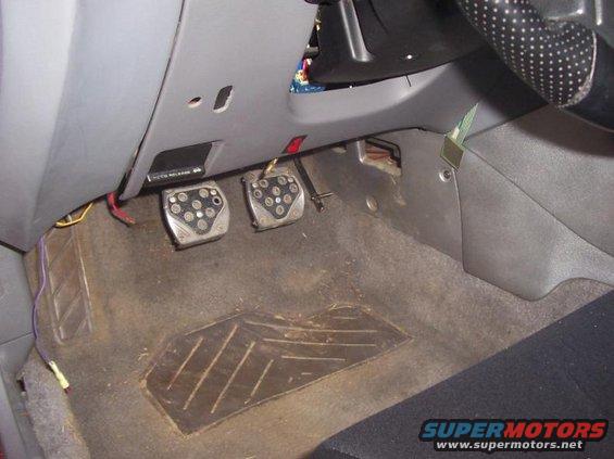 Car interior with aftermarket pedals and worn carpet. Wires are visible near the pedals