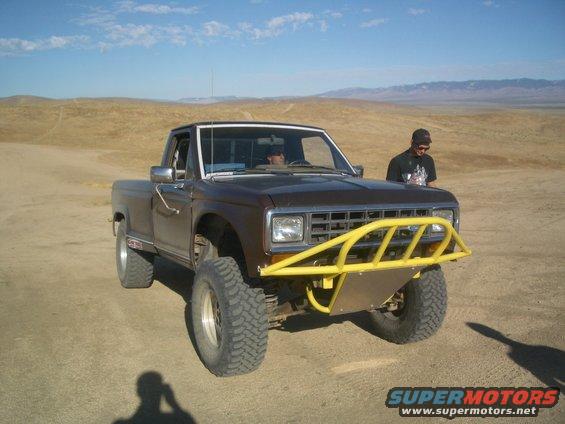 Brown pickup truck with yellow bull bar and off-road tires parked in a desert landscape