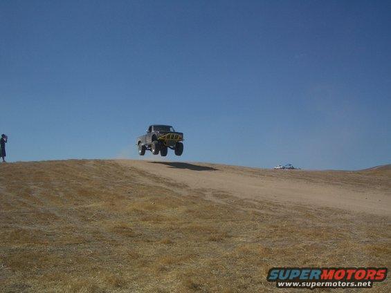 1985 Ford Ranger mid-air over a dirt hill with a person standing on the left