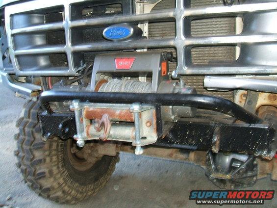 Front view of a white Ford Bronco with a chrome grille, a WARN winch mounted on a black aftermarket bumper, and a large off-road tire
