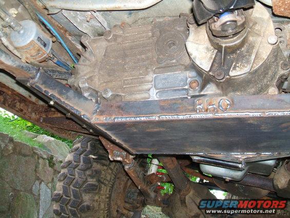 Underbody view of a vehicle's transfer case and custom skid plate. Tires and suspension components are visible