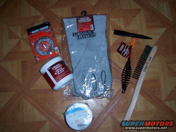 Welding gloves, grinding discs, wire brush, and other welding supplies laid out on a wood-patterned floor