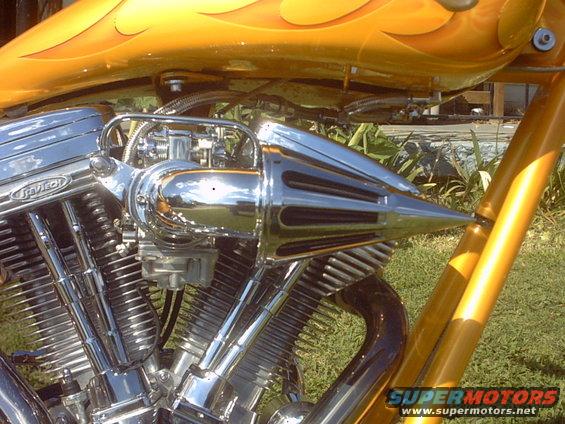 Close-up of a chrome air intake and V-twin engine on a custom motorcycle with orange flame paint