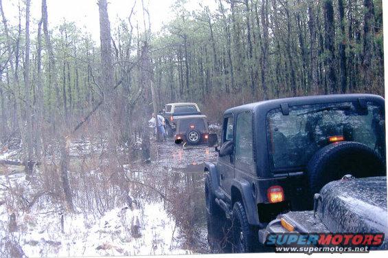 Black Jeep Wrangler rear view, driving on a muddy forest road with snow patches