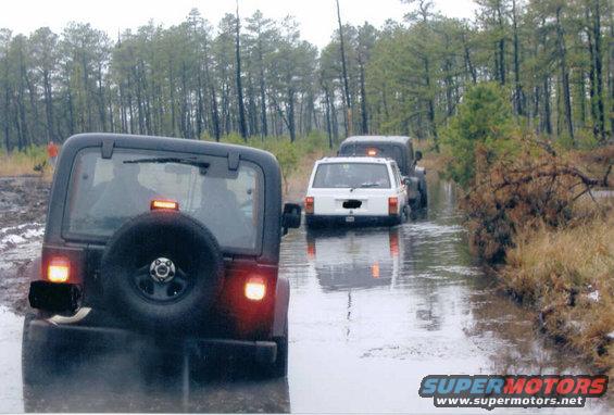 Rear view of a 1997 Jeep TJ driving through water, with other Jeeps behind