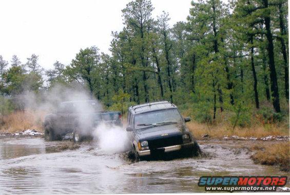 Jeep Cherokee XJ driving through mud and water with another vehicle behind it