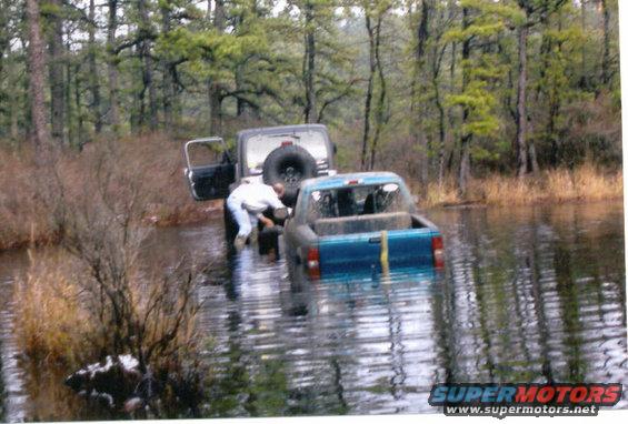 Two off-road vehicles partially submerged in water with trees in the background