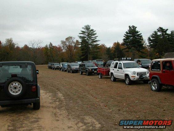 Several Jeeps parked in a line on a dirt road, with trees in the background