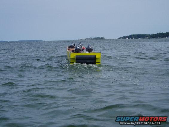 Yellow boat with four outboard motors moving away on the water