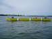 1978 Ford F-250 - A yellow floating barrier with outboard motors moves across the water, with buildings visible on the distant shore.