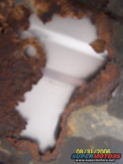 rusted metal panel with a hole showing white interior structure. Date stamp 08/31/2006
