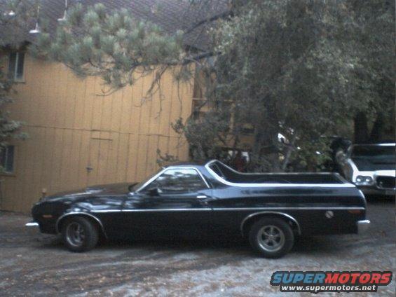 Black 1972 Ford Ranchero parked on gravel, side view. Another vehicle is partially visible to the right