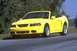 2003 Ford Mustang - A bright yellow 2003 Ford Mustang convertible is captured in a three-quarter front view on a paved road.