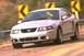 2003 Ford Mustang - A silver 2003 Ford Mustang is captured in motion on a winding road, with directional signs visible in the background.