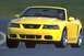 2003 Ford Mustang - A yellow 2003 Ford Mustang convertible is shown from the front, driving on a road with a driver visible.
