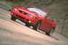 2003 Ford Mustang - A red 2003 Ford Mustang convertible is captured in motion on a winding road.