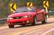 2003 Ford Mustang - Red 2003 Ford Mustang convertible driving on a road with yellow curve warning signs in the background.