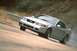 2003 Ford Mustang - A silver 2003 Ford Mustang is captured in motion on a winding road with a guardrail visible in the background.
