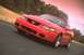 2003 Ford Mustang - A red 2003 Ford Mustang convertible drives on a road with trees in the background.