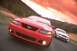 2003 Ford Mustang - Two Ford Mustangs drive on a road with a dramatic sunset sky.