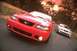 2003 Ford Mustang - A red 2003 Ford Mustang leads a silver Mustang on a winding road at sunset.