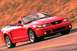 2003 Ford Mustang - A red 2003 Ford Mustang convertible is captured in motion on a blurred background.