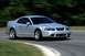 2003 Ford Mustang - Silver 2003 Ford Mustang coupe captured in motion on a paved road with blurred green foliage in the background.