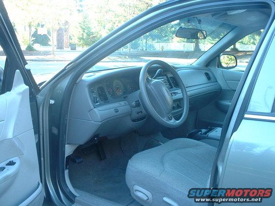 Interior view of a car's dashboard, steering wheel, and front seats. The driver's side door is open