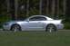 2003 Ford Mustang - A silver 2003 Ford Mustang coupe is captured in motion on a grassy field, with trees blurred in the background.