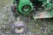 1987 Ford Bronco - Close-up view of a green riding mower's engine and front wheel, resting on gravel and grass.