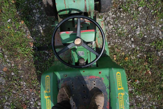 Green riding mower interior with black steering wheel and worn foot pedals. Text reads GENERAL PURPOSE