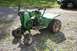 1987 Ford Bronco - A green riding mower sits on a gravel driveway next to a dark car.