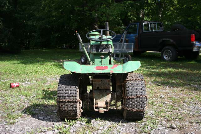 Green riding mower with chains on rear tires, parked near a black pickup truck