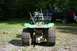 1987 Ford Bronco - Rear view of a green riding mower with tire chains, with a black pickup truck in the background.