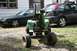 1987 Ford Bronco - A green riding mower sits in front of two cars parked on a gravel driveway.