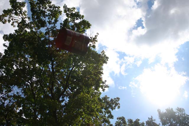 Red can flying against a blue sky with clouds and trees