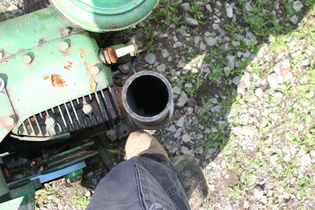 Close-up of an exhaust pipe on a green engine. A person's leg and foot are in the foreground