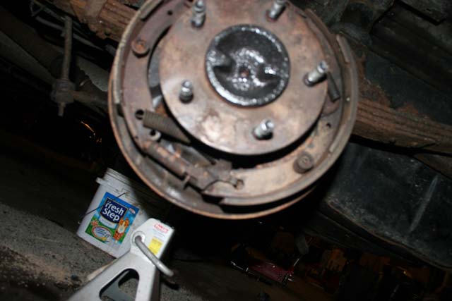 Drum brake assembly with rusty components, jack stand, and a bucket of cat litter