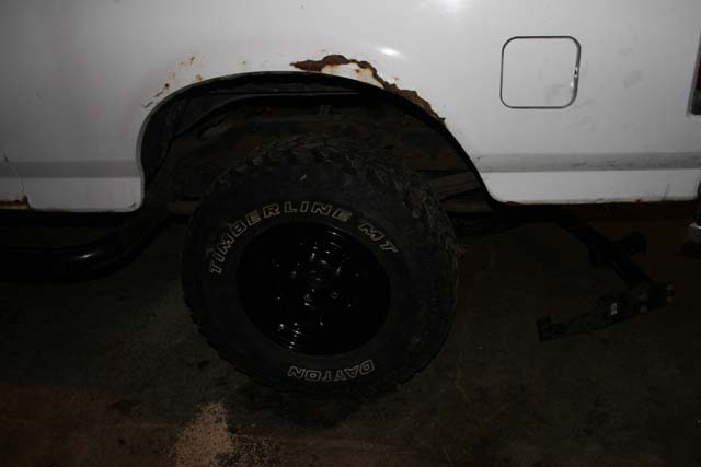 White vehicle's rear wheel well with rust, black tire, and fuel door