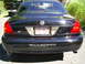 2003 Mercury Marauder - The rear of a black 2003 Mercury Marauder sedan is visible, with a black pickup truck parked behind it on a sunny day.