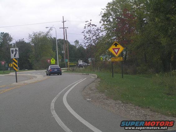 Blue sedan driving on a road with yield signs and a school crossing sign