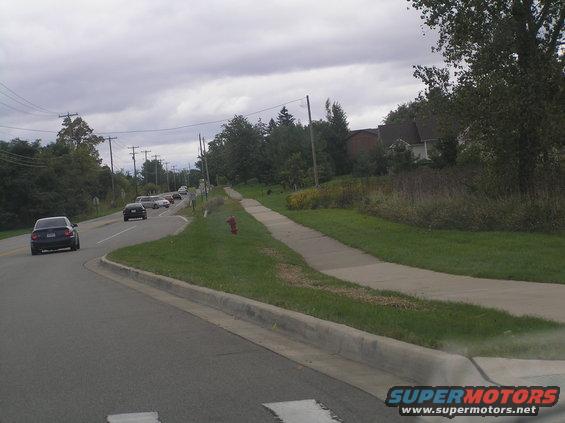 Dark sedan driving on a road with other cars and houses in the background