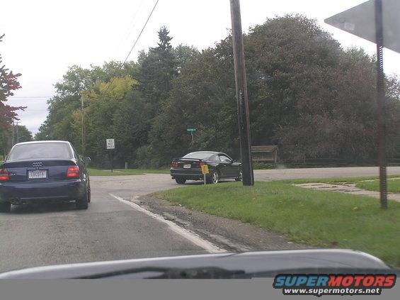 Dark sedan and black coupe on a tree-lined road